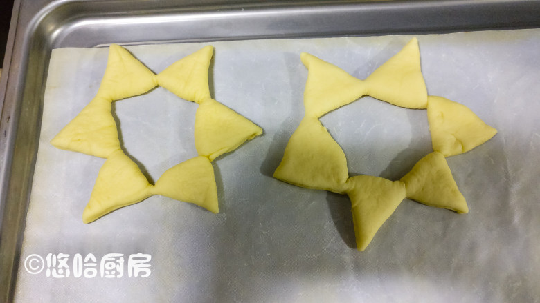 圣诞树面包,在面团上压出痕迹的地方,用刮板从面团中心依次切开,但是都不要切断,将所有的切口全部展开,衔接的地方稍微捏一下,避免散开。这个操作最好是在烤盘上进行,在案板上整形操作好了,移到烤盘上的时候,极为容易散开。依次做完全部面团,面团之间留有空隙,摆放在烤盘上。2份20克的面团,擀开后压出五角星的形状,用刮板切出五角星待用。