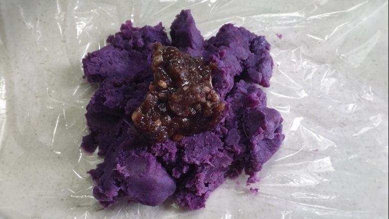 颜色艳丽的紫薯茶巾绞,给餐桌上加点不一样的色彩,取一小块的紫薯泥,放在保鲜膜上,压平加入适量的红豆沙