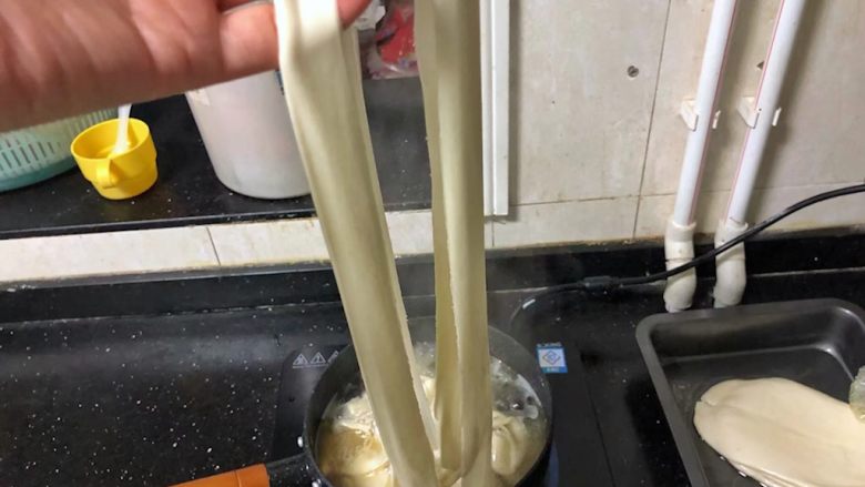 河南小吃-羊肉烩面,17、把面胚抻长后从中间的压痕一分为二,放入锅中。