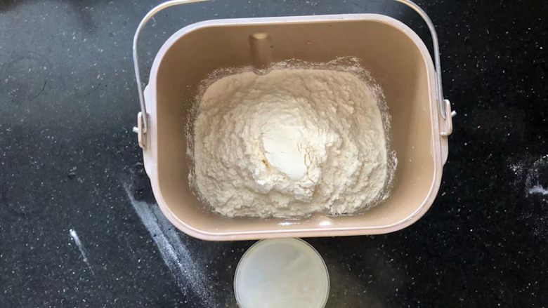 河南小吃-羊肉烩面,7、接下来制作烩面的面胚。把食用碱和盐倒入温水中融化,面粉放入面包机中。