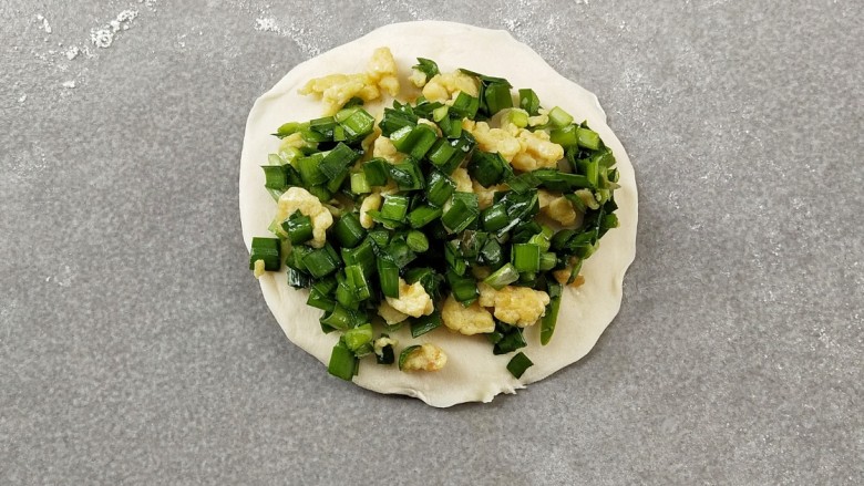 韭菜盒子,取一块面团,撒上少许的干粉防粘,用擀面杖擀成四边薄,中间厚的面片,再放上馅料。