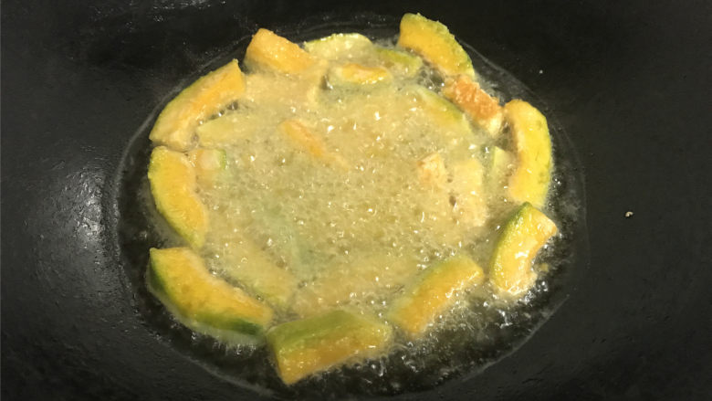 咸蛋黄焗南瓜,锅中倒入适量的油,把裹上淀粉的南瓜条放入锅中,炸至表面呈金黄色后捞出。