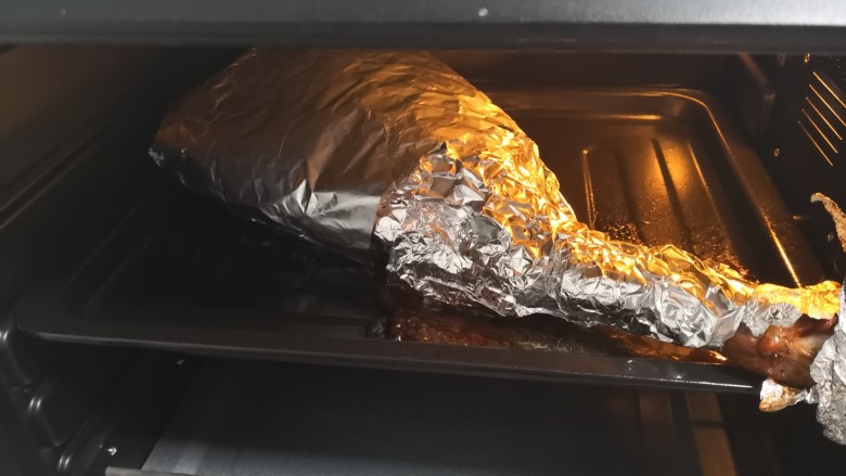 烤羊腿,24小时后取出羊腿撕掉保鲜膜,更换成锡纸将羊腿完整包裹(上下各一层锡纸),放入烤箱上下火200烤制40分钟。