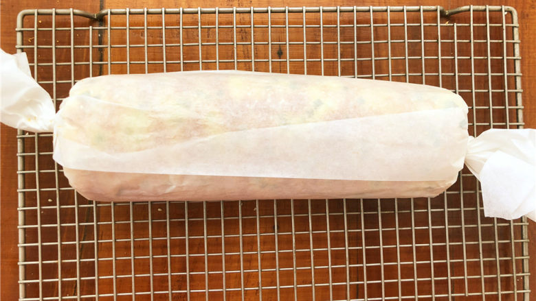 香葱肉松面包卷,趁着余热把面包卷起来,用油纸包裹之后拧紧两边固定一下,放凉以后再打开。