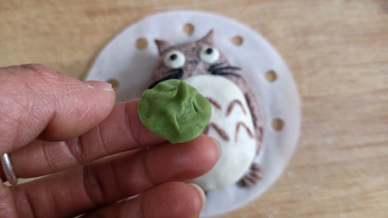 卡通龙猫豆沙包,用白色面团做龙猫肚皮,眼睛胡须鼻子用取少量白色面团加一点点<a style='color:red;display:inline-block;' href='/shicai/ 211839'>竹炭粉</a>来做,将龙猫表面涂薄薄一层水,将做好的配饰粘上。