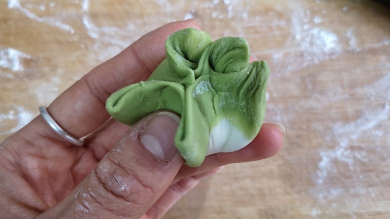 八宝百财蒸饺,把五星每一边用右手拇指指肚向中心推,形成菜叶状纹理,然后压至五星的下一边,依次完成。