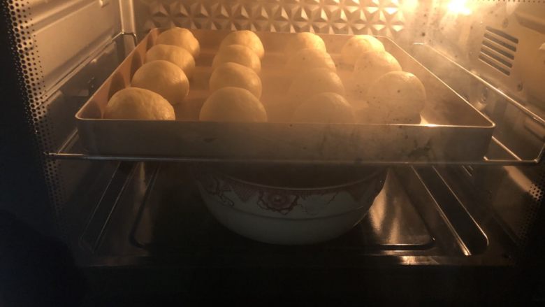 椰蓉小餐包,把烤盘放入烤箱里利用烤箱自动发酵功能把面团发酵成原来的1.5到2倍大,在下面或者旁边放一盘热水,保证面团的湿度和温度。