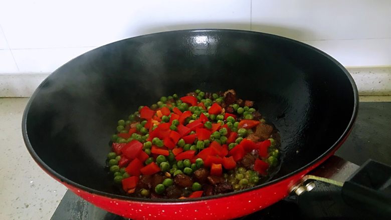 小炒腊肉丁,下入洋葱、姜蒜,翻炒约1分钟出香味时倒入豌豆和柿子椒,翻炒2分钟,放盐,炒匀。