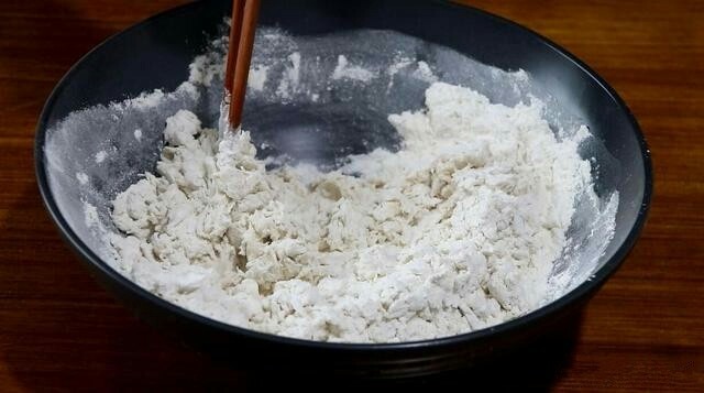 香甜红糖锅盔,将酵母水倒入面粉中,边倒边用筷子搅拌。