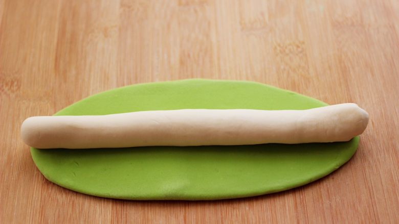 长长久久的翡翠白玉牛肉萝卜饺子,把静置好的两个颜色面团,白色的面团搓成长条,绿色的面团擀成椭圆形,把白色的长条放在上面。