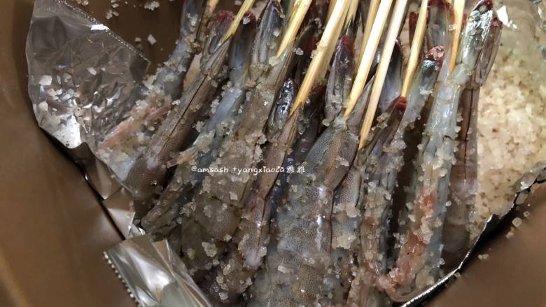 五香盐焗虾,把混合好的一半海盐倒入面包机桶中,然后把串好的虾也摆入面包机中,如果竹有点长可以剪短点,这样子后面面包机的盖子才可以盖得上
