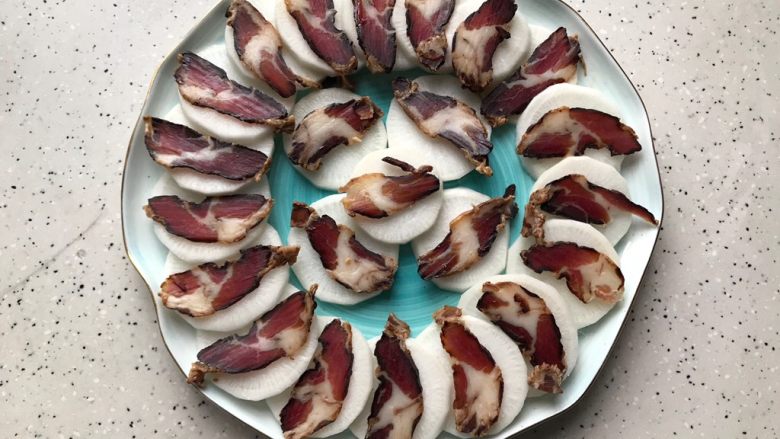 萝卜蒸酱油肉,然后如图所示,将萝卜一片一片绕着盘子边缘叠起来,再在每片萝卜上摆放上酱油肉