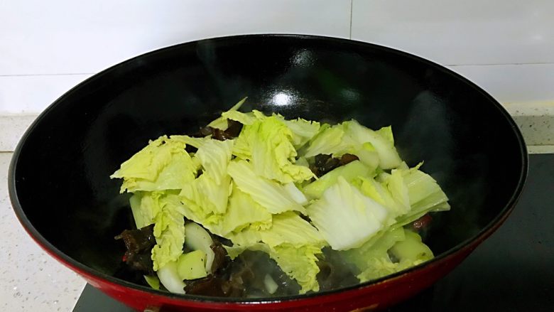 大白菜炒木耳,放入白菜叶子,一面炒一面加入盐,放入葱叶,翻炒均匀。