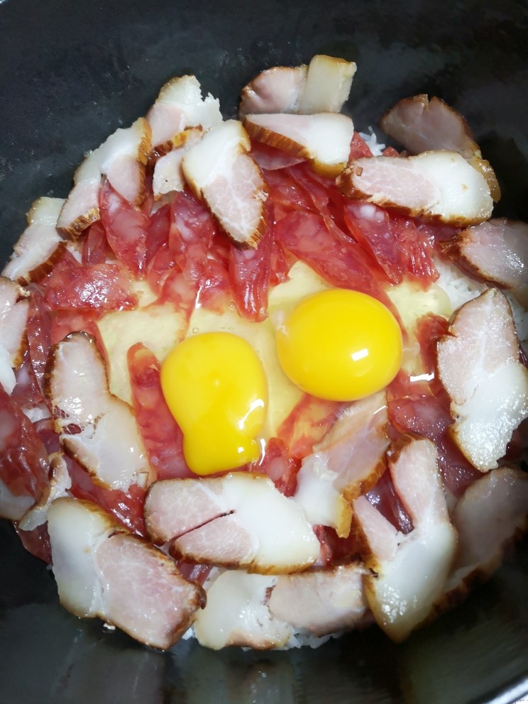 双腊煲仔饭,米饭九成熟加腊肉腊肠,打入两个<a style='color:red;display:inline-block;' href='/shicai/ 9'>鸡蛋</a>,盖上盖子继续小火焖几分钟,如果肉量少可以沿锅边淋少许油,以防糊锅