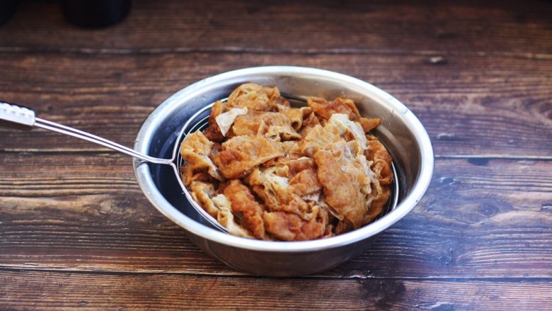 虾仁笃面筋(天津菜),用汤勺压一压笊篱里的面筋,把面筋控干水份备用。