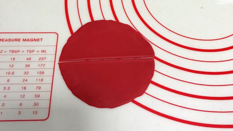 小福猪中国结馒头,取12克红色面团,揉匀排气滚圆,擀成圆形薄片,中间一切为二。