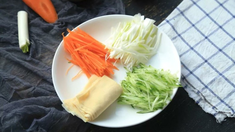 京酱肉丝,2.大葱、胡萝卜、黄瓜洗净切成细丝备用,薄百叶在热水中浸泡10分钟,然后切成巴掌大小的方形,并将它们整齐的码放在盘子上;