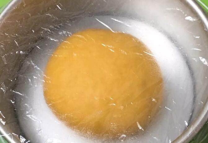 南瓜豆沙味喜饼,厨师机揉面至面粉结团,无需出膜状态。揉面完成整理、滚圆放入模具,盖上保鲜膜。
