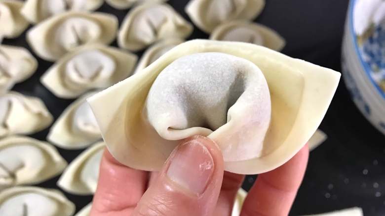 荠菜馄饨,再在两个角的边上蘸点水抹上,把两边捏在一起,成为元宝型状。