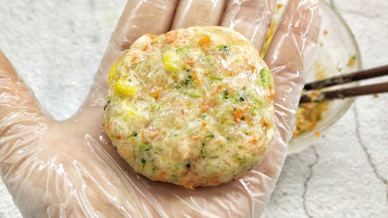 鸡胸蔬菜饼,手带一次性手套,抺少许的油防粘,取一团放入掌心,将其压扁成饼状