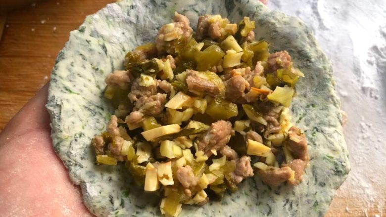野菜团子,先把每片柚子叶刷上一层薄薄的油,放在盘里待用,揪一小块面团下来,用擀面杖擀成面皮,放入馅料,包起来,把包好的野菜团子放到柚子叶上面,依次把全部包好(我包了二种形状的)。
