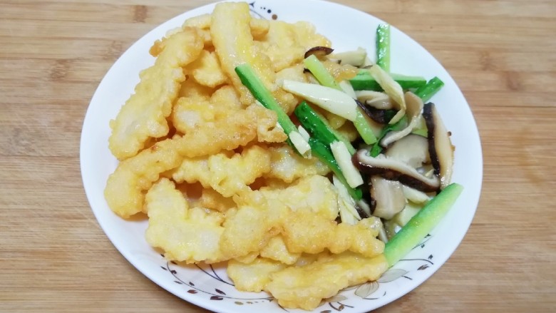 金牌官烧目鱼,将目鱼条均匀的裹上炸糊下入,炸至金黄色后,倒入冬菇、冬笋、黄瓜和木耳汆一下,一并倒入漏勺沥油备用。