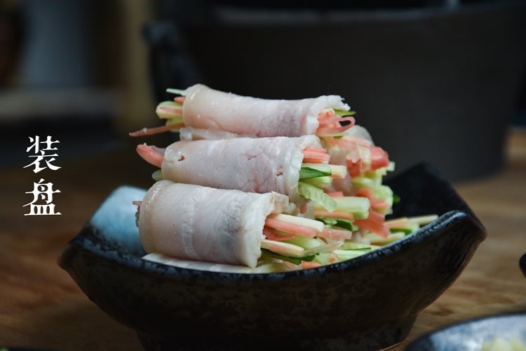 蒜泥白肉卷,五花肉平铺于菜墩上,黄瓜丝、胡萝卜丝依次放入肉片上,卷成卷,装盘。