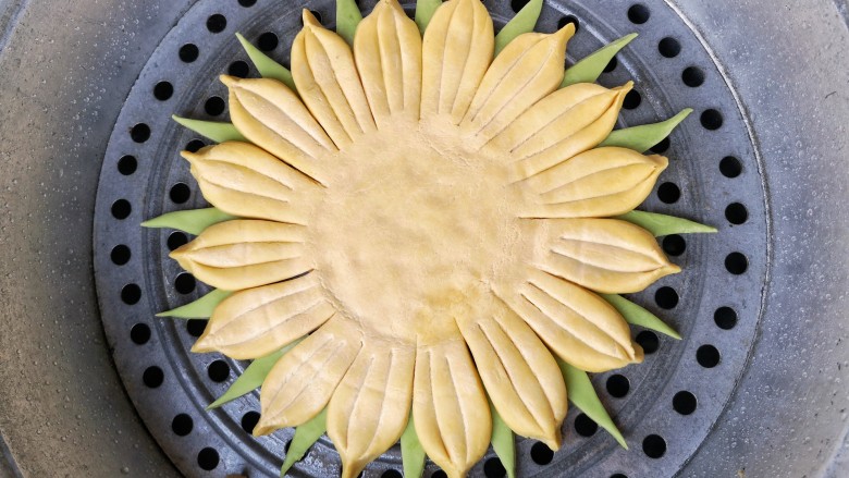 春暖花开,把菠菜面团做成的三角用水贴在葵花盘子造型花瓣空隙处做叶片,并放在抹了薄油的篦子上,上锅隔水大火蒸20分钟,关火后闷3分钟,出锅。