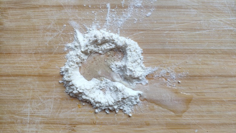 土豆造型豆沙包(馒头),取5—10克面粉放在面板上,加入一点点酵母,倒入少许水,和成一块小的白面团。(用来制做土豆芽)