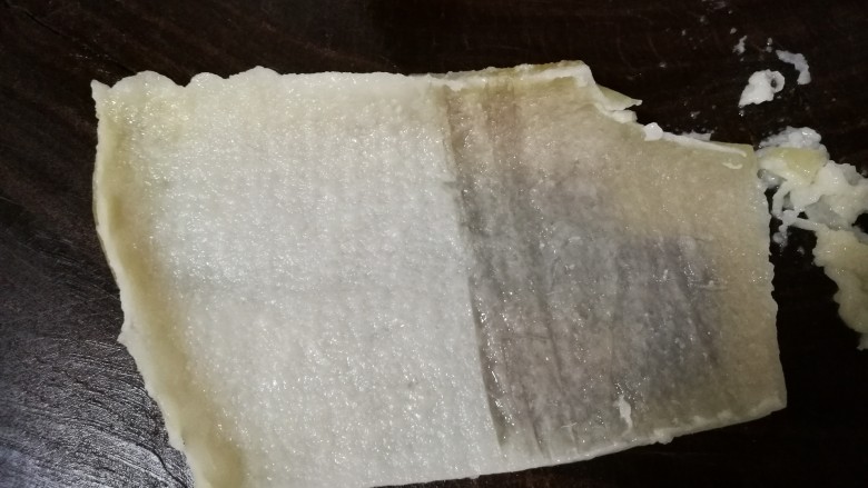 豆皮猪皮冻,将煮好的肉皮平铺在菜板上,里层有油脂的一面朝上,用刀反复刮去上面的油脂。要想皮冻清爽不腻,这是关键一步,必须把油脂仔细刮干净。