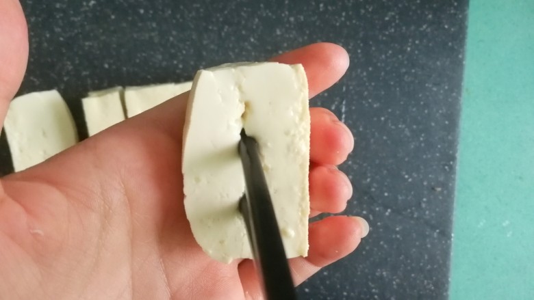 客家美食《砂锅煲咸菜酿豆腐》,取一块豆腐,用筷子在豆腐中间夹个缝