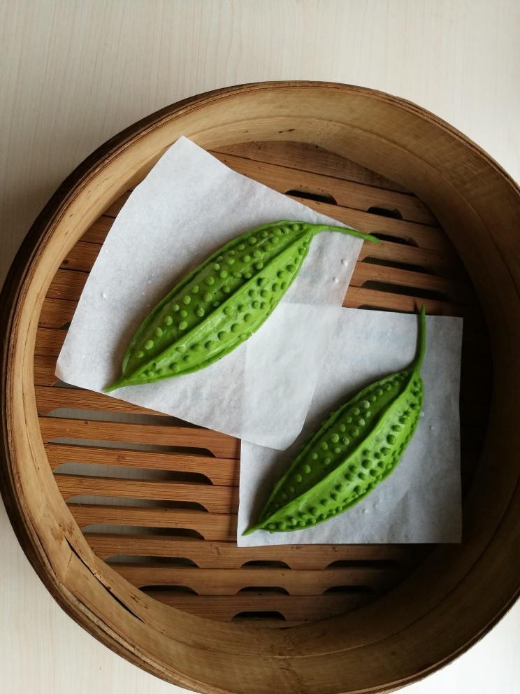 造型馒头——苦瓜豆沙包,蒸锅放入35º左右的温水,将做好的苦瓜放入笼屉内,盖上锅盖醒发。当看到苦瓜变成原来的1.5倍大,用手指轻轻按压表面后能慢慢的回弹,拿起来感觉变得比刚做好时轻,就表示醒发好了。这时可以开火蒸制,上汽后蒸15分钟,关火后过5分钟揭盖。