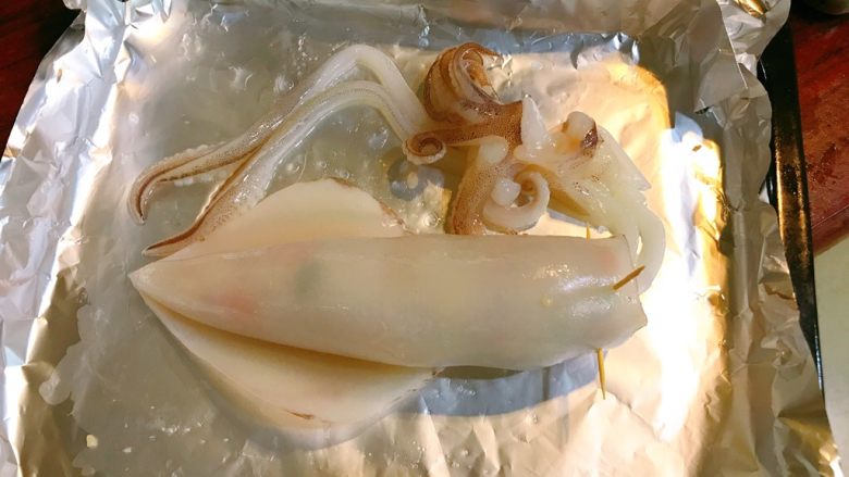 烤鱿鱼包饭,封口处用牙签固定住。烤盘上炒一层油,放在烤盘上。