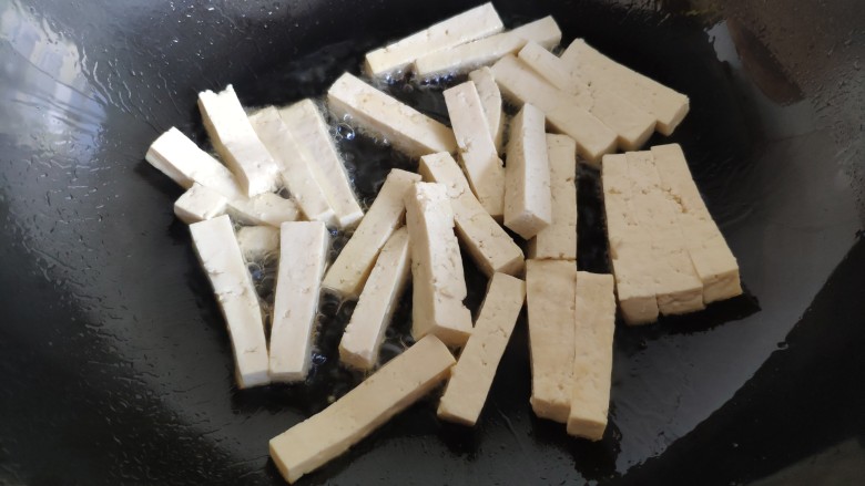 蒜薹炒豆腐,炒锅油热后,放入豆腐条。不要马上翻动它,把火调小一点,慢慢地来煎豆腐条。最好用不粘锅更容易些。