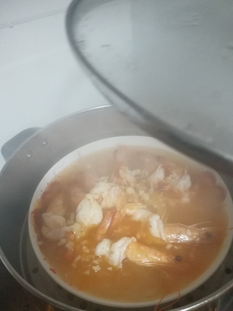家烧虾,打开蒸锅锅盖,冒着蒸汽呢,小心烫,把蒜末均匀潵在虾上,然后淋上热油,把你刚才锅里煮的玉米油都淋上去。
