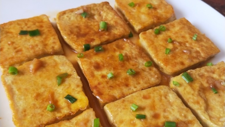 锅塌豆腐,盛盘,把汤汁浇在表面,撒葱花点缀。