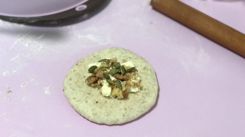 全麦奶酪果仁软欧(老面法),稍擀扁擀圆后放上适量奶酪馅和果仁碎。
