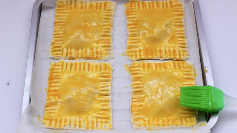 馄饨皮香蕉派,烤盘铺油纸放入做好的香蕉派,表面刷上蛋黄液。