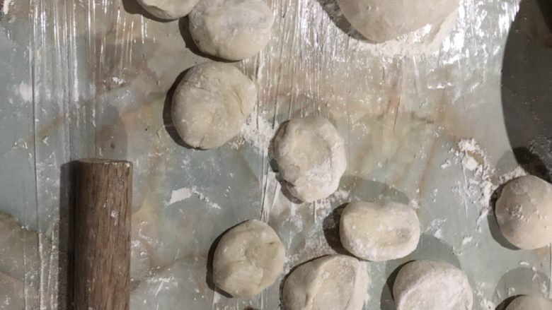自制豆沙包,操作台铺保鲜膜充当揉面垫。面团分成两半,其中一半搓长,切成小剂子,用手按压一下,变成饼状。