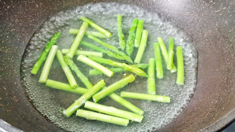 芦笋培根卷,锅里水开放入几滴油和适量的盐, 将芦笋放入里面去焯水。