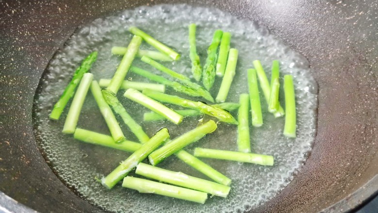 芦笋培根卷,锅里水开放入几滴油和适量的盐， 将芦笋放入里面去焯水。