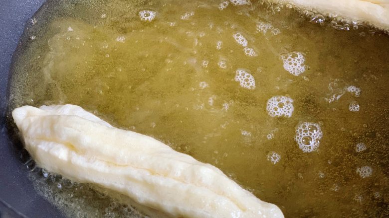 酵母版油条,锅内倒入适量玉米油,烧至7成热时,用手捏住油条胚头尾两端,轻轻拉长扭一下放入锅里。