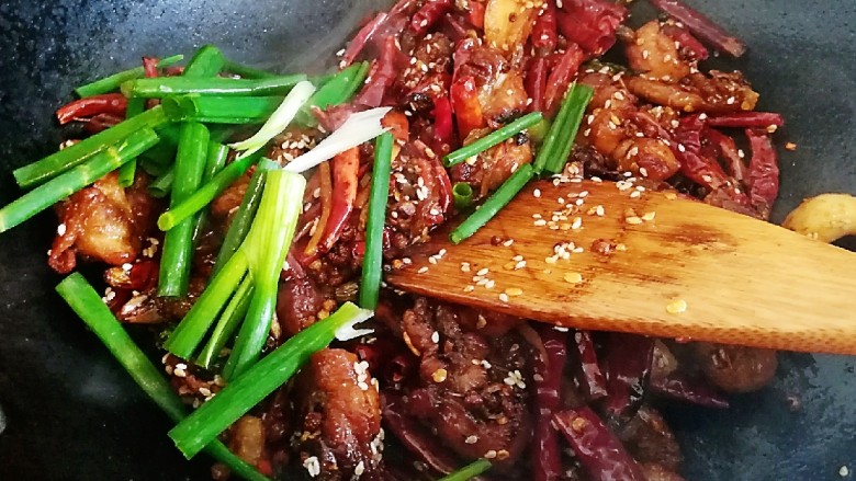 椒香辣子鸡,撒上白芝麻,倒入葱段,翻炒均匀,停火起锅