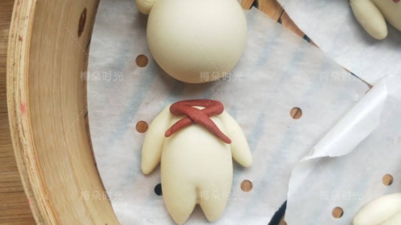 红领巾小熊馒头,取10克面加入少许红曲粉,揉成红色面团,取2克左右,搓成长条。做红领巾。先把头部移开,如图环绕脖子的位置交叉在胸前。