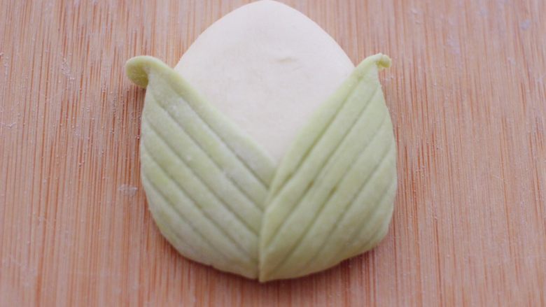花样粽子馒头,把两片叶子沾少许清水后,粘到三角白面团上,左边一片,右边一片,交叉着捏紧后整一下型。