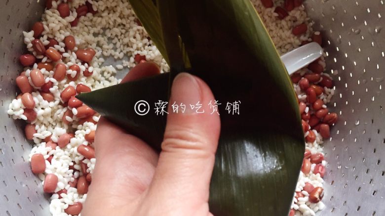 赤豆三角粽,把另一边的粽叶翻过来,盖住斗里的糯米,大拇指和食指捏紧粽身的的左右两端,成为一个三角形。