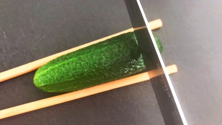 风味酱香乳瓜,取一个小乳瓜,在乳瓜的两侧放上筷子,用刀切成连刀片