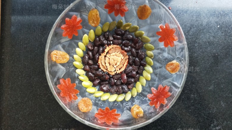 蜜汁八宝饭,取一个小碗,刷上猪油,红枣花摆中心,再摆入蜜红豆,再摆上南瓜子。碗的边壁摆上果丹皮,葡萄干。