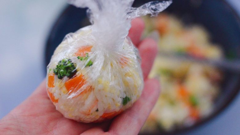 阿根廷红虾时蔬二米饭团,把搅拌好的饭团食材,取适量的饭团食材,放入保鲜膜里,借助保鲜膜,把饭团弄成圆团。
