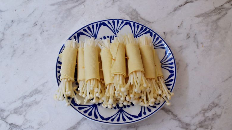 豆皮金针菇卷,取一张豆皮,再将金针菇放入,再从一边卷起来,最后用牙签固定住,依次做完所有的豆皮